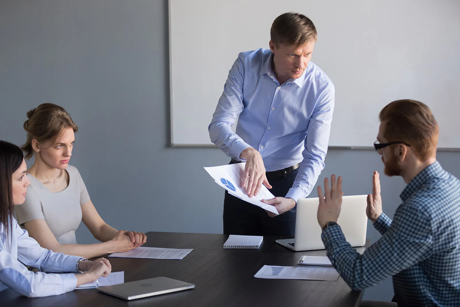 En una sala de juntas un supervisor agita papeles mientras habla con un empleado que se ve intimidado